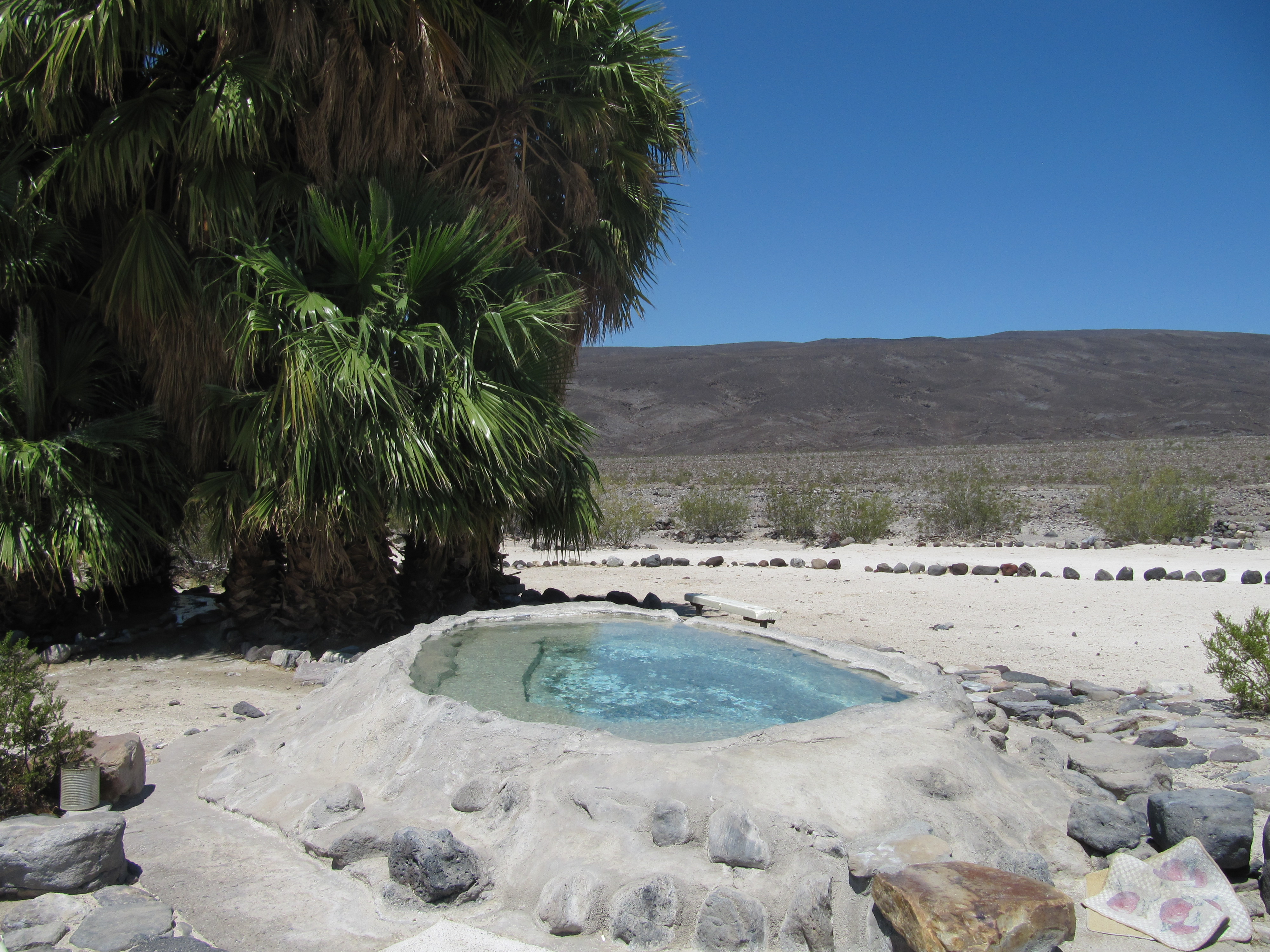 A man-made concrete-lined pool is visible surrounded by a few palm trees and bare ground.