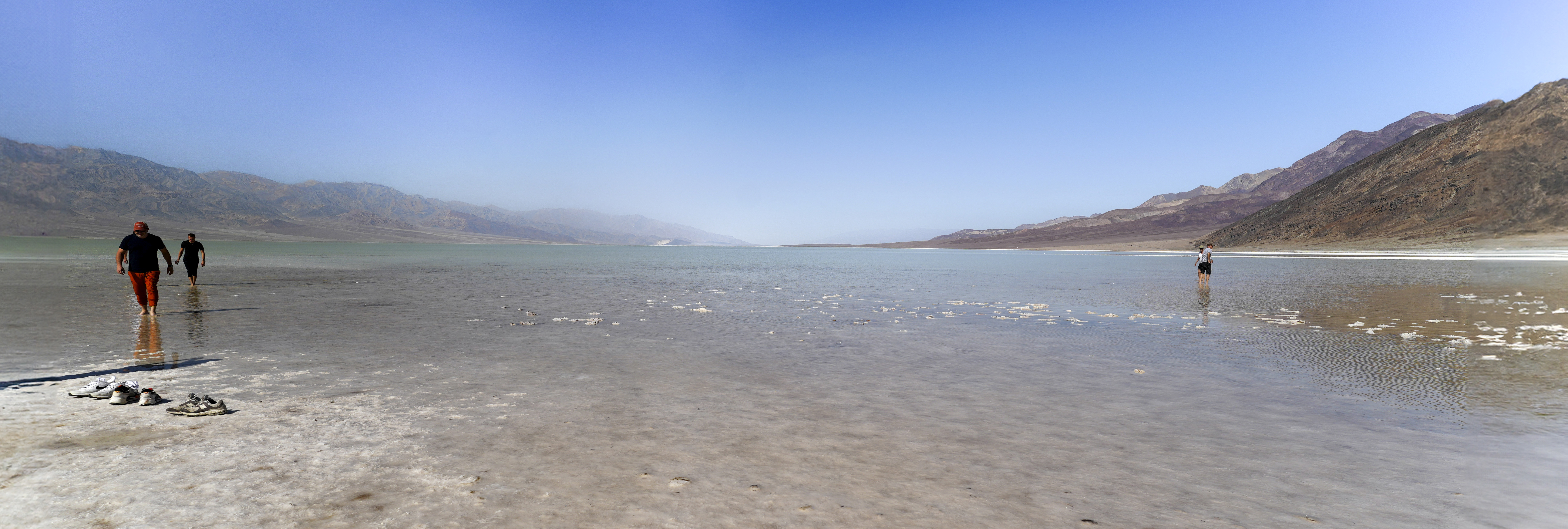 White salt flat in the foreground with a shallow body of water extending across the field of view, with mountains on the edges.