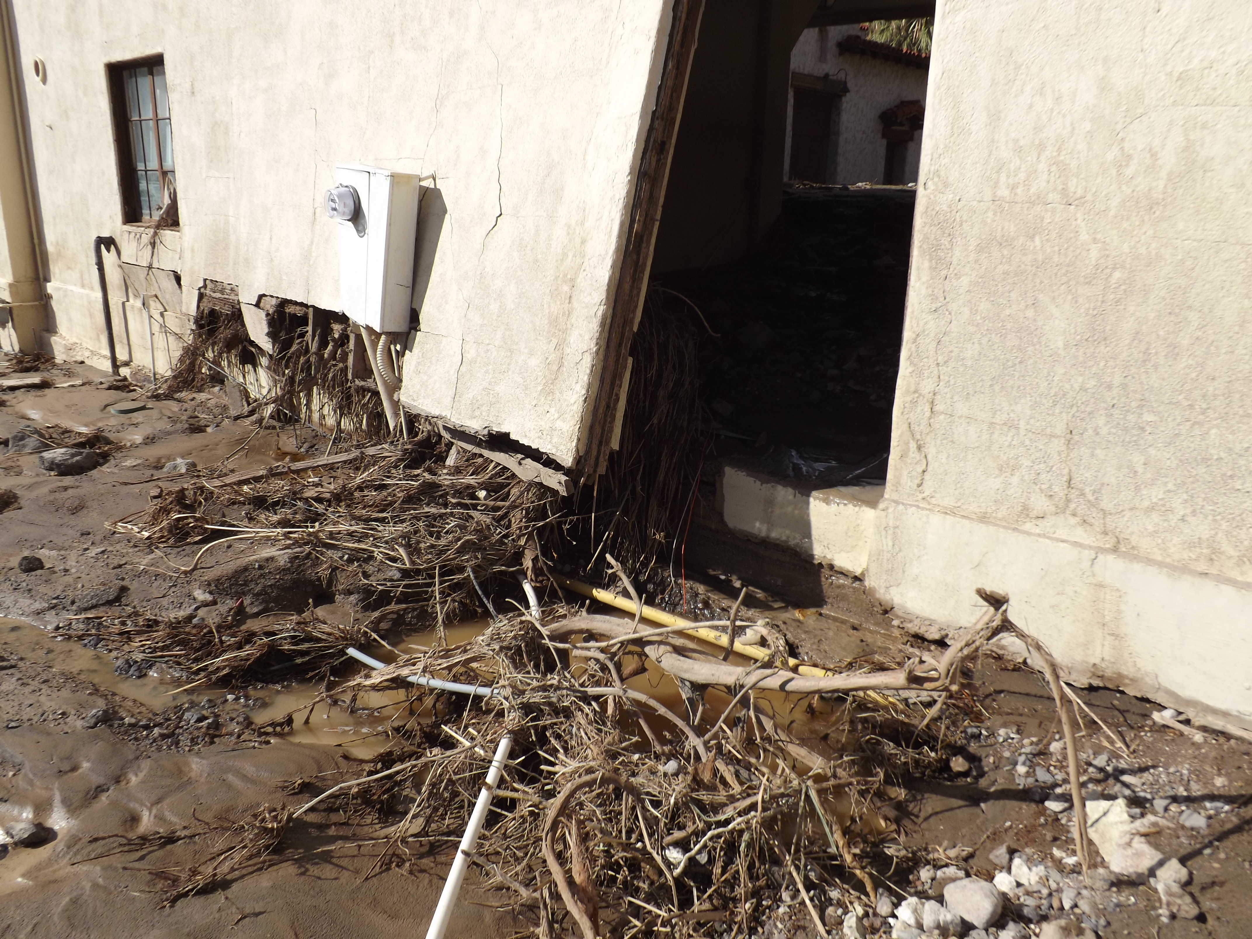 Rocks, soil and other flood debris litters the front of a long, damaged building.