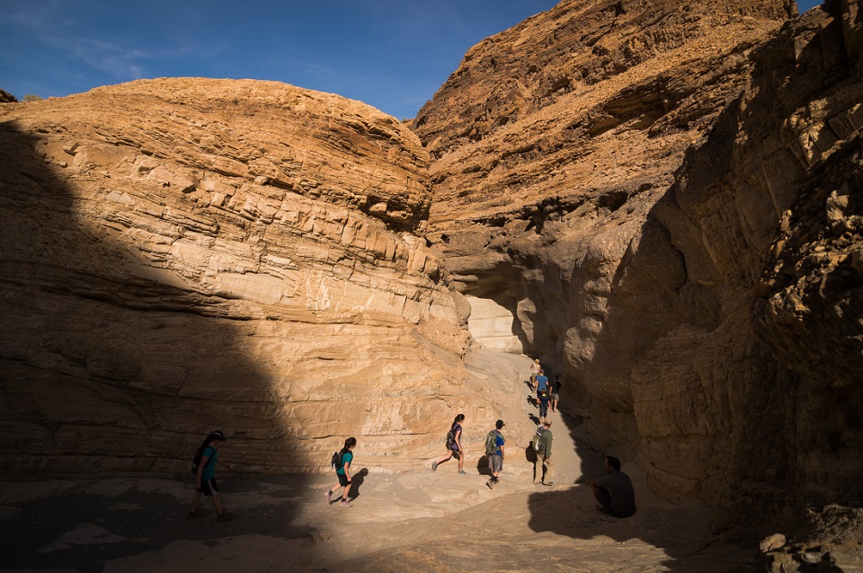 Hikers walk uphill in Mosaic Canyon. The canyon walls in sunlight are bright, but the shaded areas are very dark.