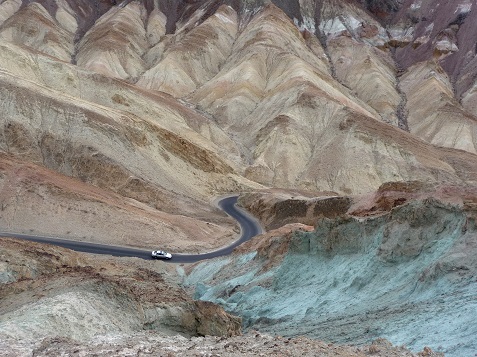 As seen from a above, a car drives the one-lane Artists Drive.