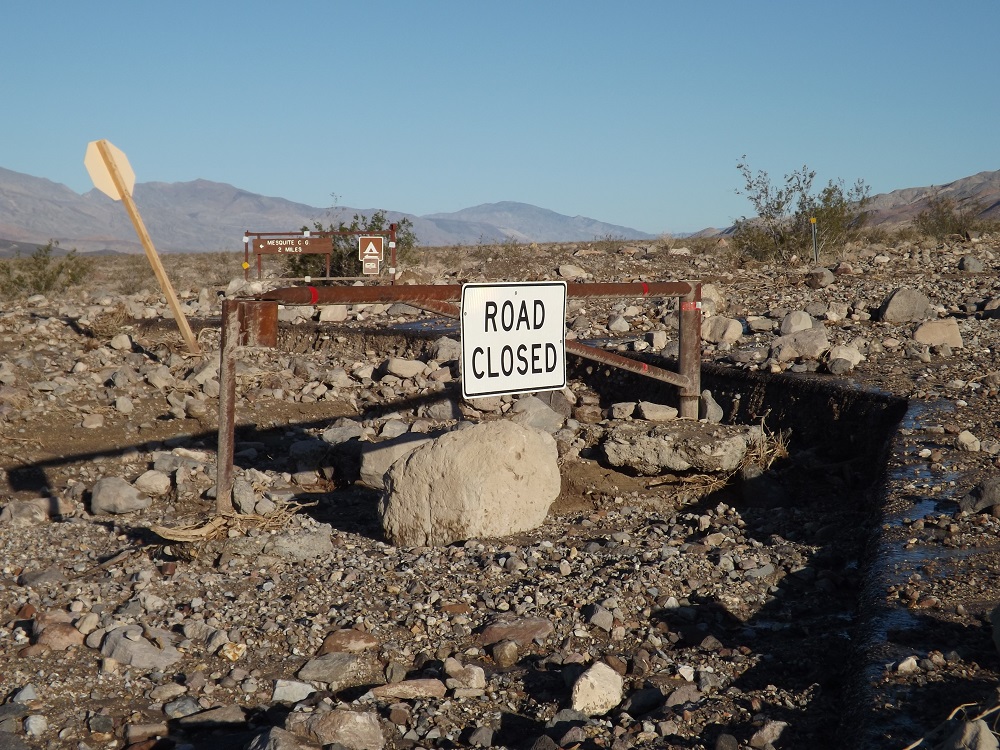 a "road closed" sign on a barricade among mud, rocks, and other flood debris