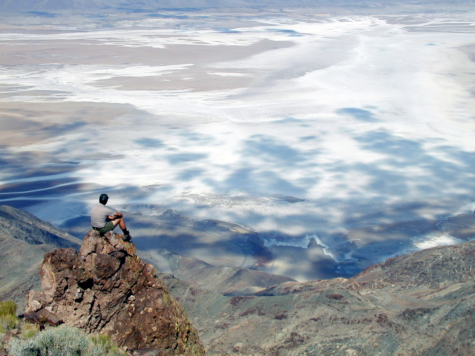 A park ranger sits on a rocky outcropping looking down on the white, flat salt flats.