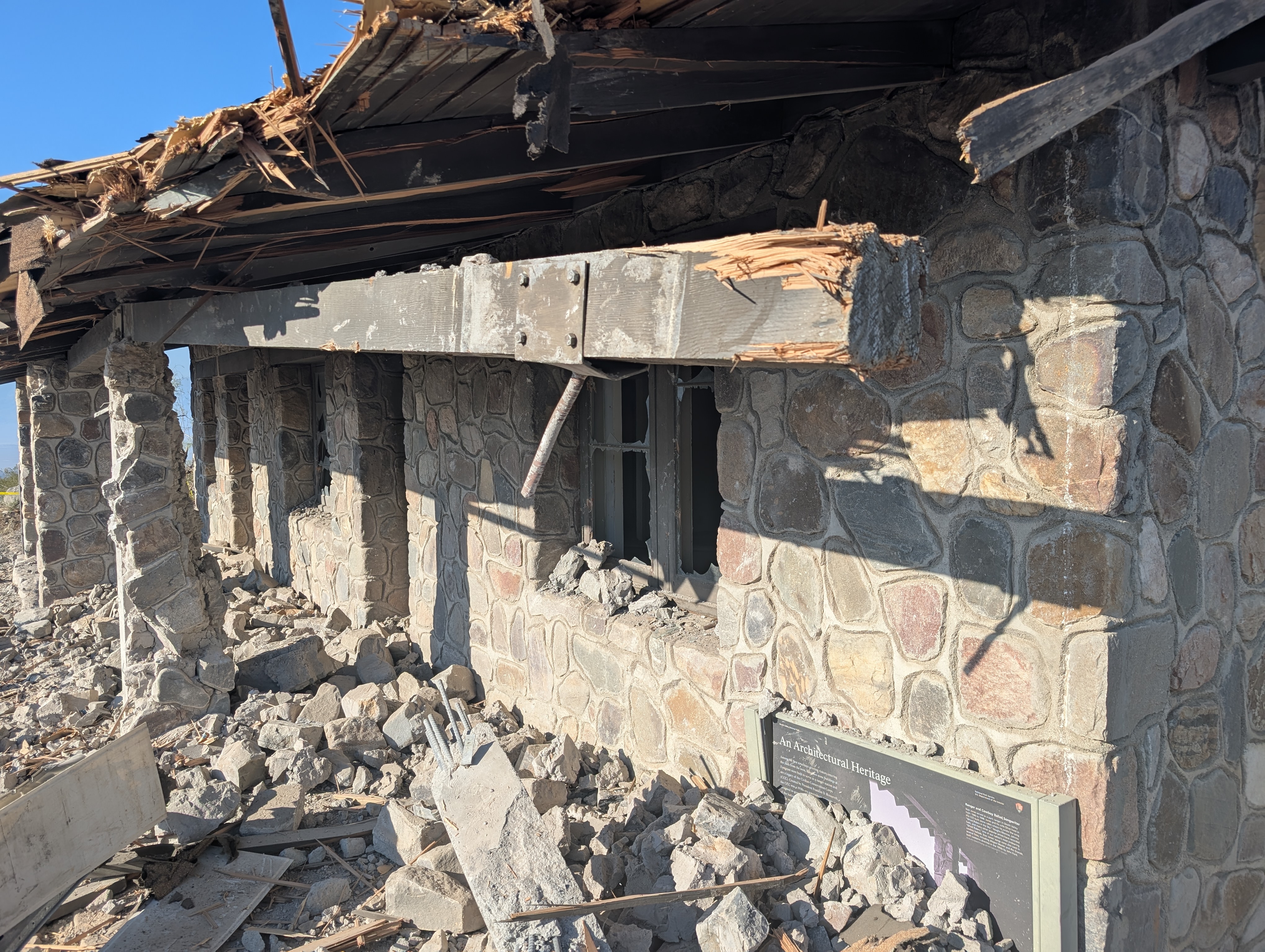 A building with stone walls has rubble, a splintered wooden roof, and broken windows.