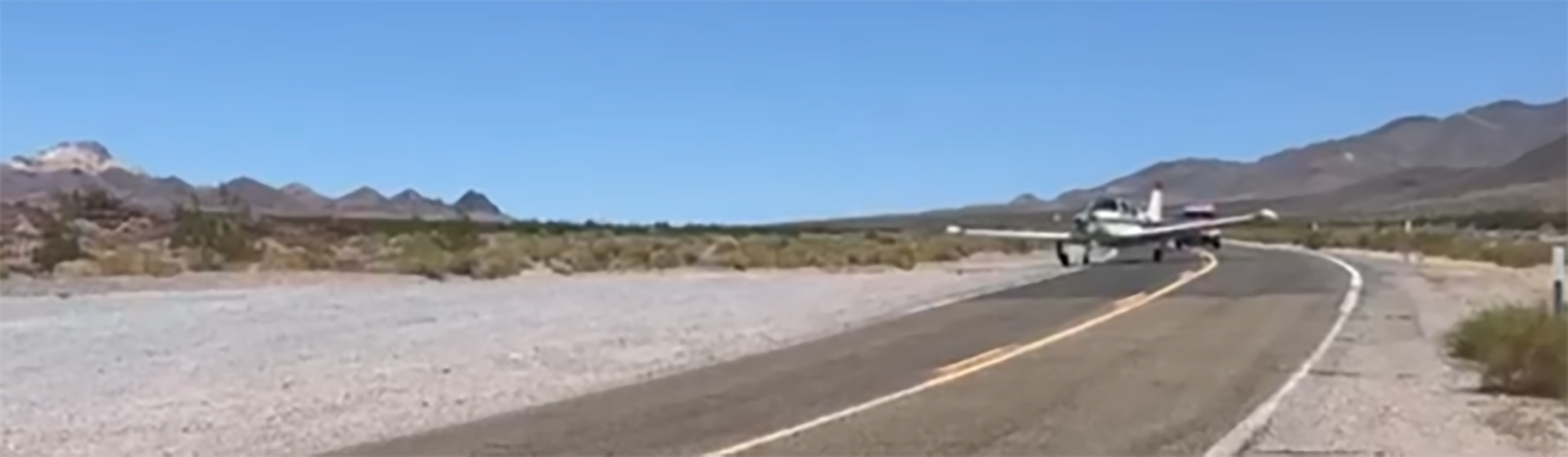 Private plane moving off CA-178 A small white airplane is on a two-lane paved road in a desert environment.