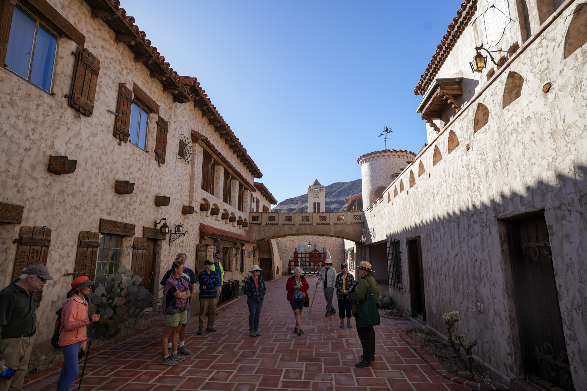 Ten people stand in a red tile courtyard facing a park ranger in green.