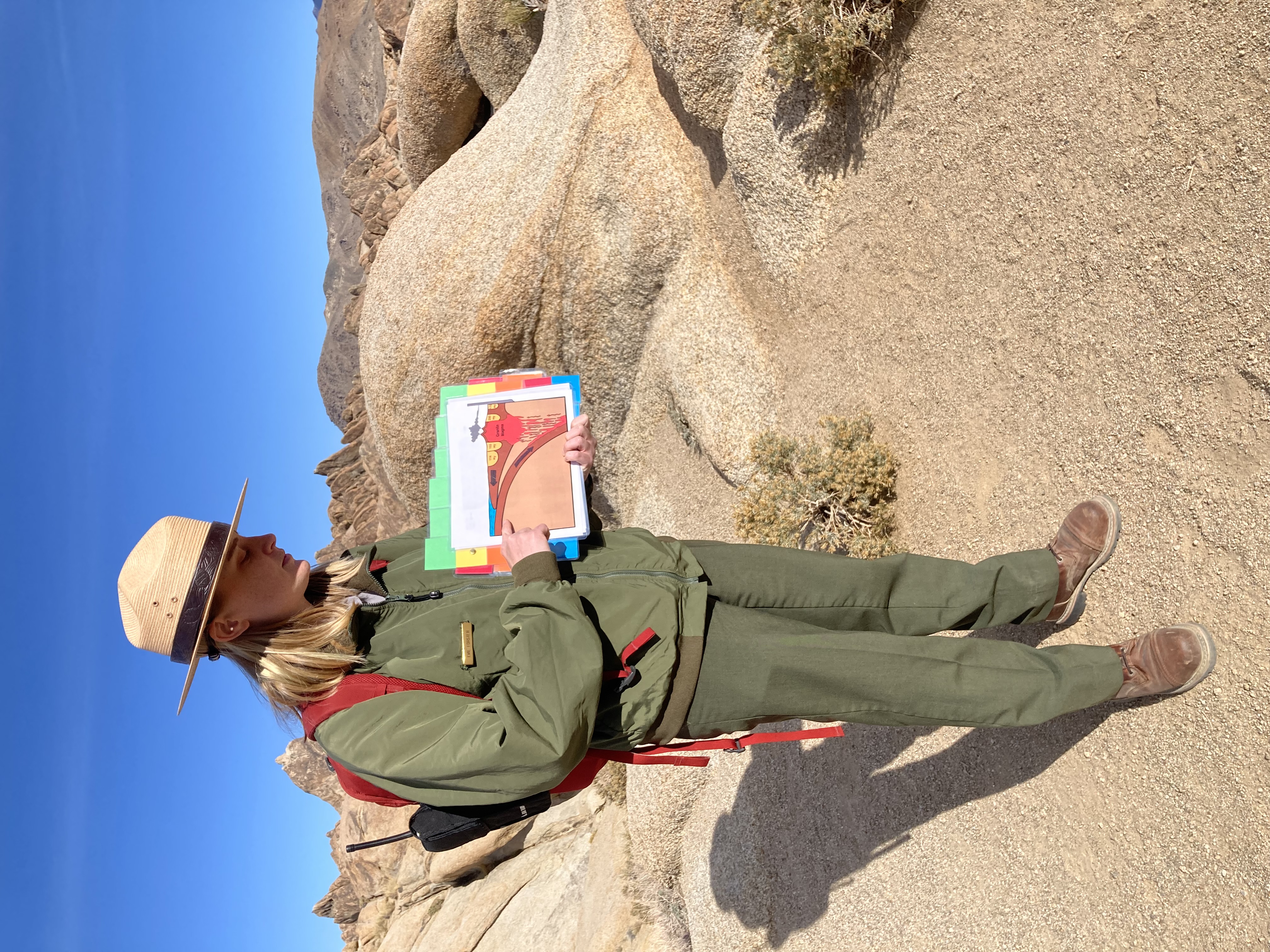 A park ranger holds a diagram showing volcanic processes in the brown granite rocks of the Alabama Hills National Scenic Area.