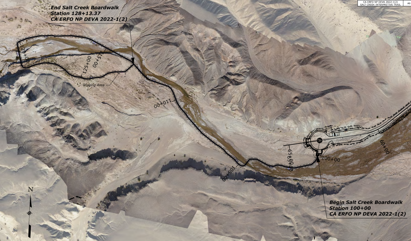 A black line shows the planned location for the road, parking lot, and boardwalk. It overlies an aerial image of a thin green ribbon between flat bare land surrounded by barren hills.
