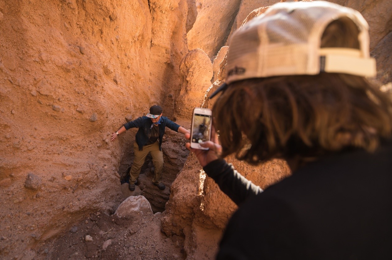 A person takes a photo of another person scrambling on tan walls.