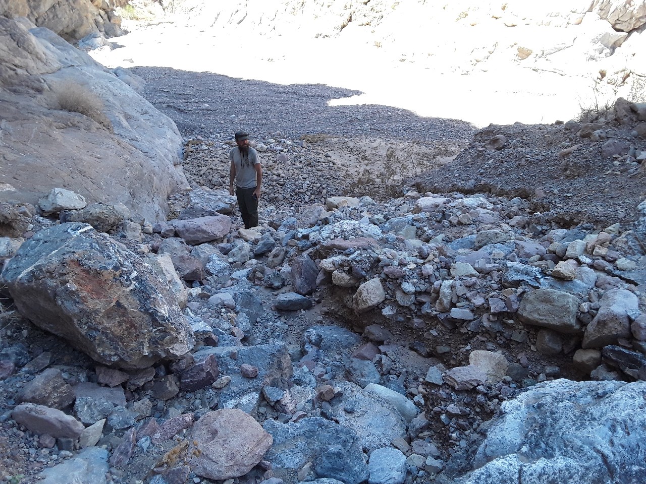 A man in green pants and gray shirt stands at the bottom of a rocky slope.