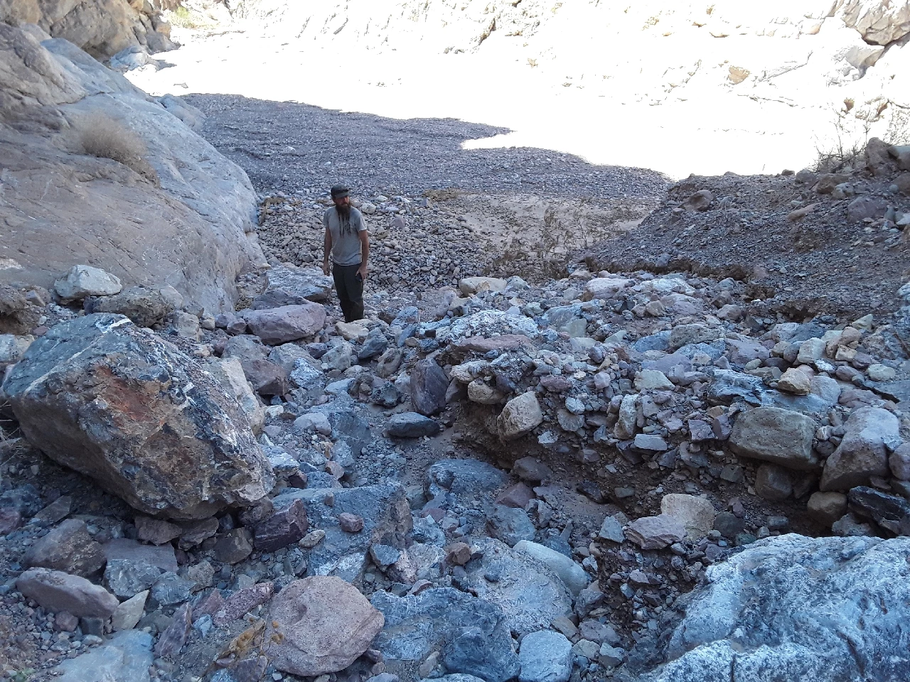 A man in green pants and gray shirt stands at the bottom of a rocky slope.
