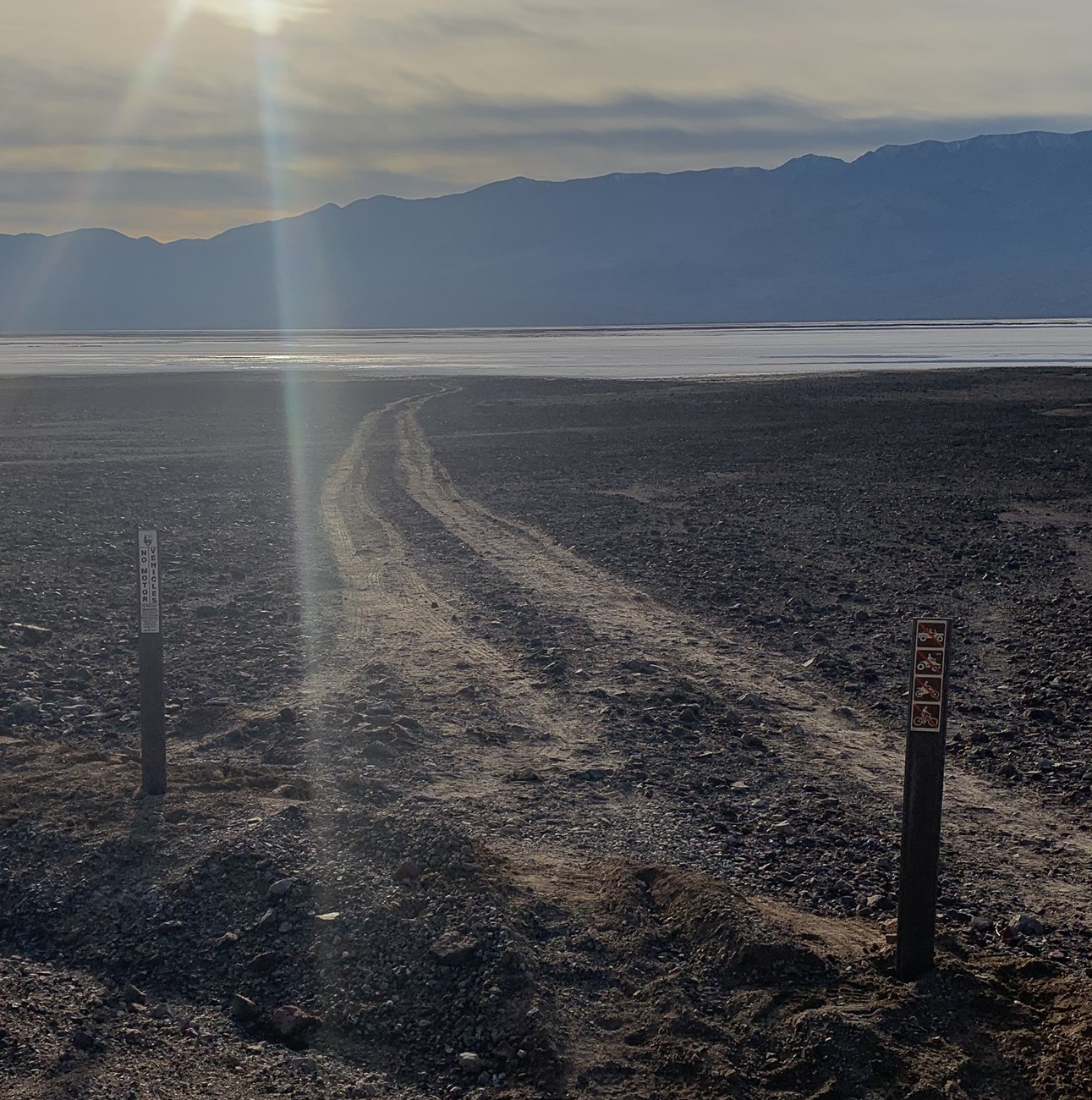 Two brown posts block off a route made by tire tracks leading to the salt flats in the distance.