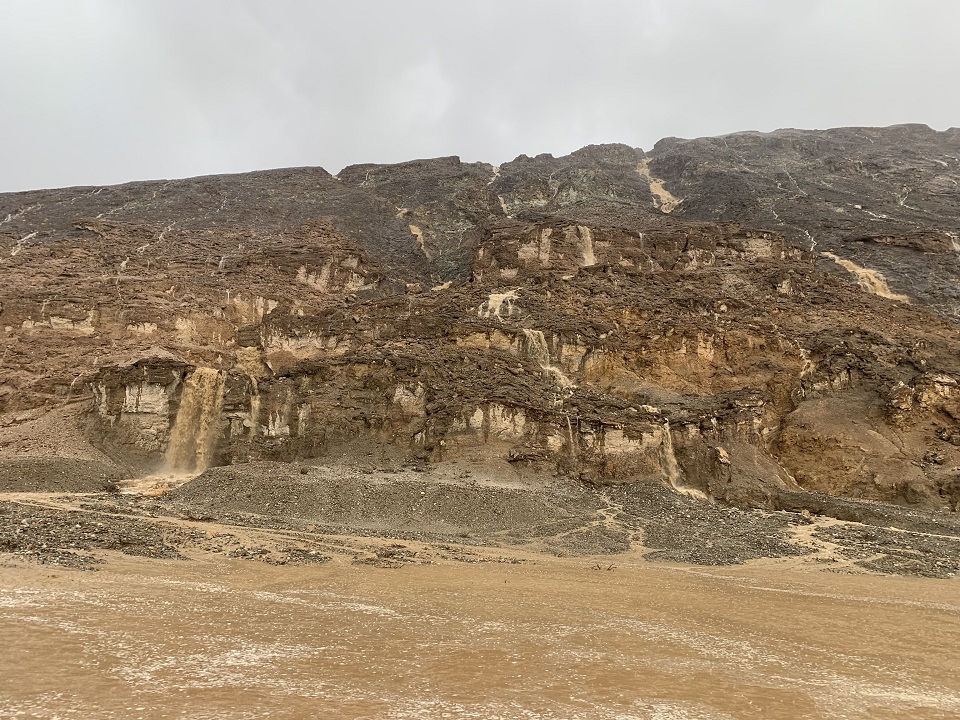 Temporary brown waterfalls cascade down a steep rocky slope under dark clouds.