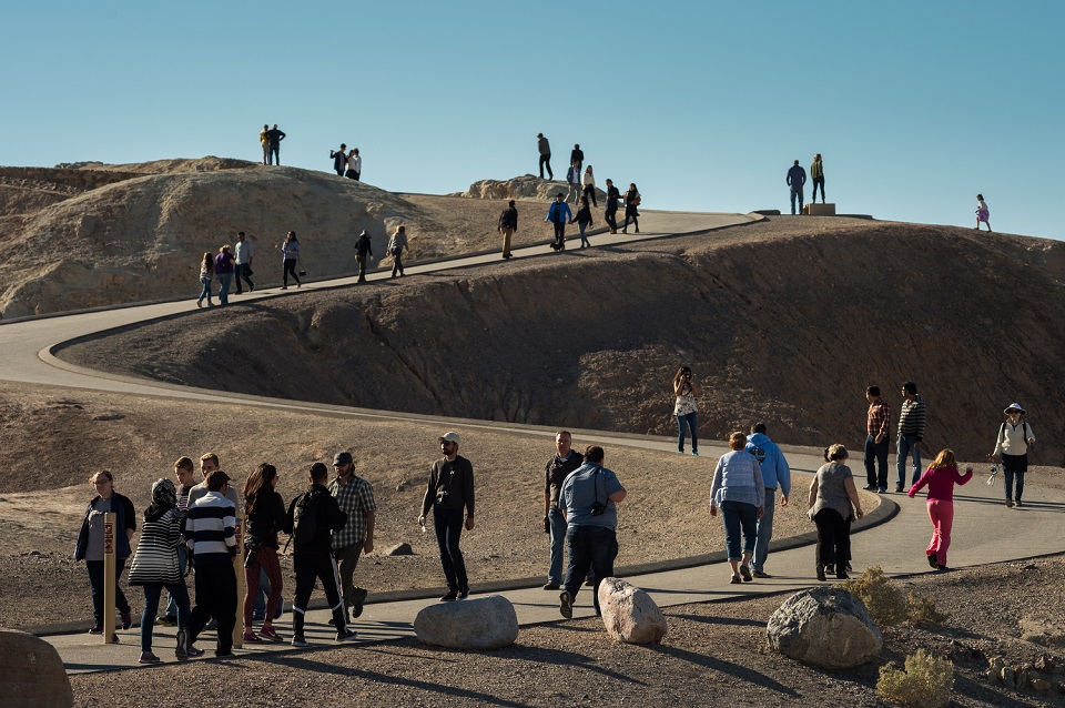 Park visitors walk up a winding paved trail to the top of Zabriskie Point.
