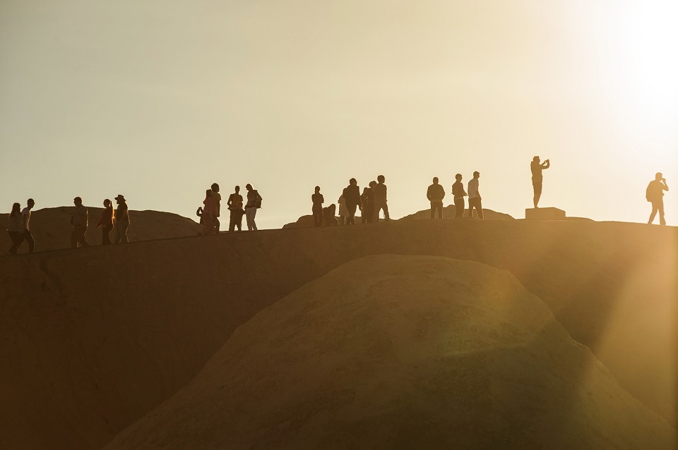 Backlit photograph shows people standing on a ridge with sun setting behind them.
