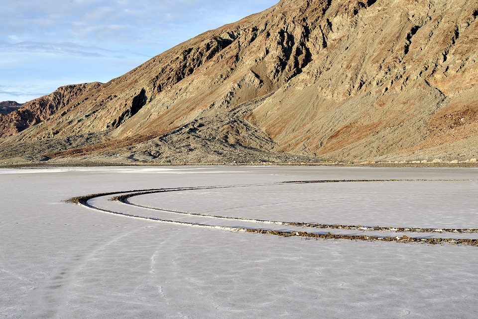 A semicircular pattern of vehicle tracks filled with water contrasts with the white salt
