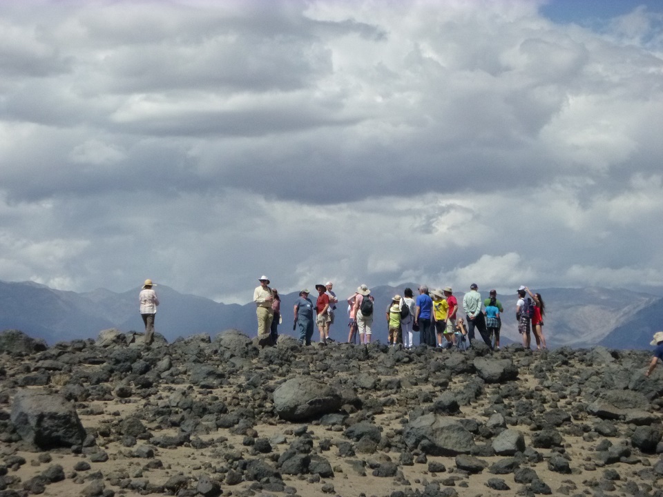 A group of visitors on a field trip about Mars research stand on a hill will dark volcanic rocks.