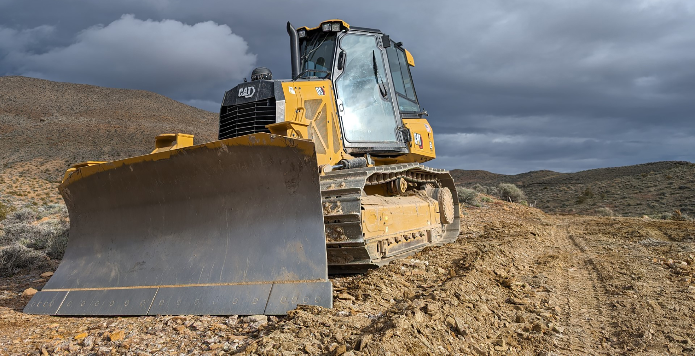 Dozer on Chloride Cliff Yellow dozer on top of brown gravel and a stormy gray sky above.
