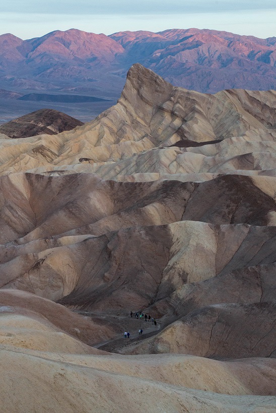 Hikers wind down a trail through highly eroded badland hills at sunrise.