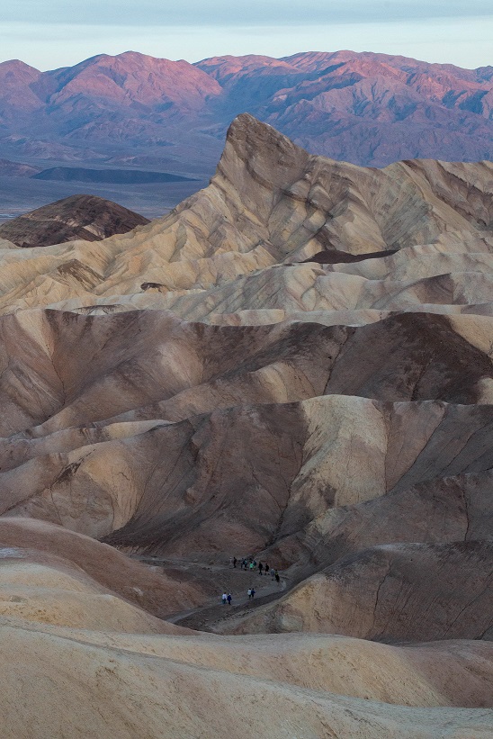 Hikers wind down a trail through highly eroded badland hills at sunrise.