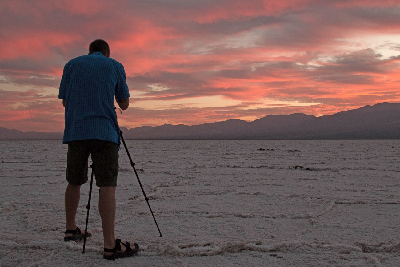 A photographer stands with a tripod on a vast salt flat.