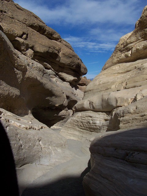 A canyon with smooth walls winds toward a blue sky.