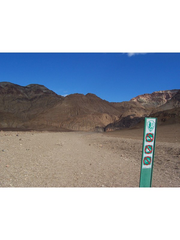 A green wilderness barrier with symbols prohibiting motor vehicles and bicycles at the start of a canyon hike.