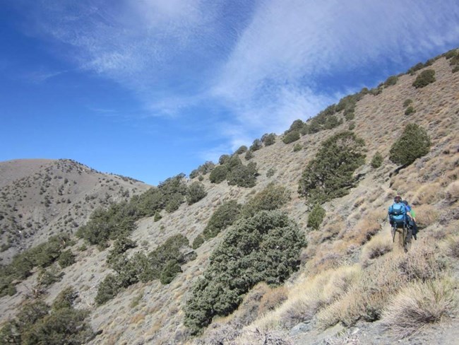Two hikers work their way along a narrow slope between two peaks.