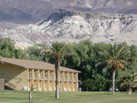 Hotel building with green grass lawn and palm trees in foreground. Mountainous scenery in background. Hotel building with green grass lawn and palm trees in foreground. Mountainous scenery in background.