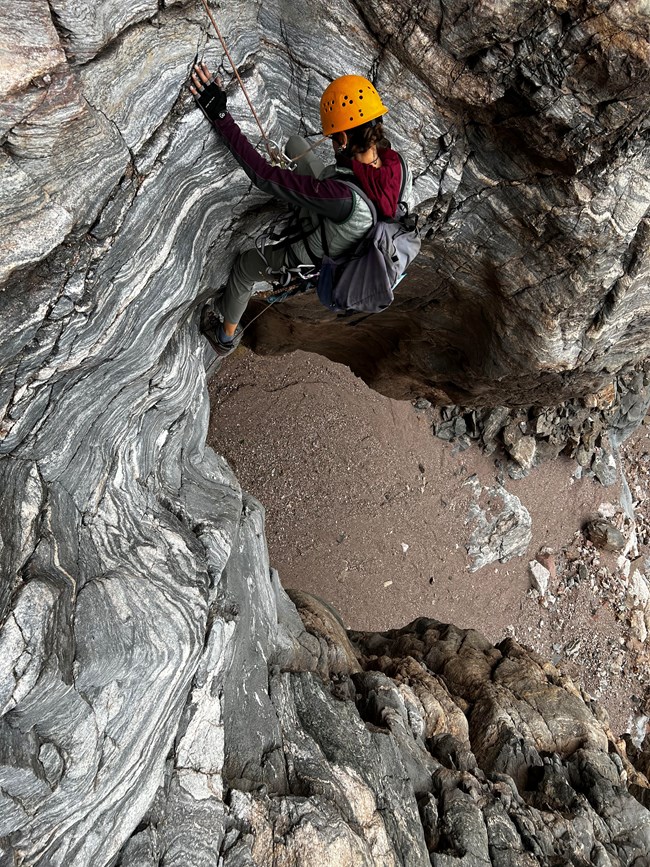 A person hanging from a rope on the side of a steep wall with black and white stripes.