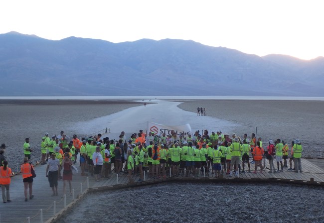 People in running gear stand waiting in a crowd on a vast salt flat.