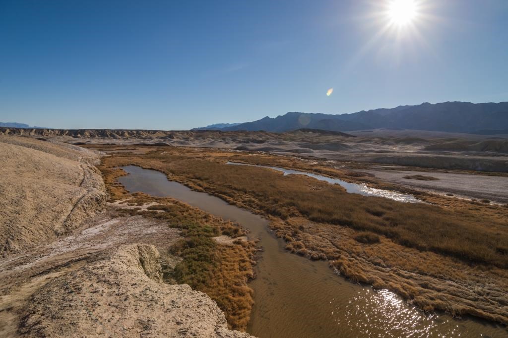 A creek runs through barren, golden colored hills.