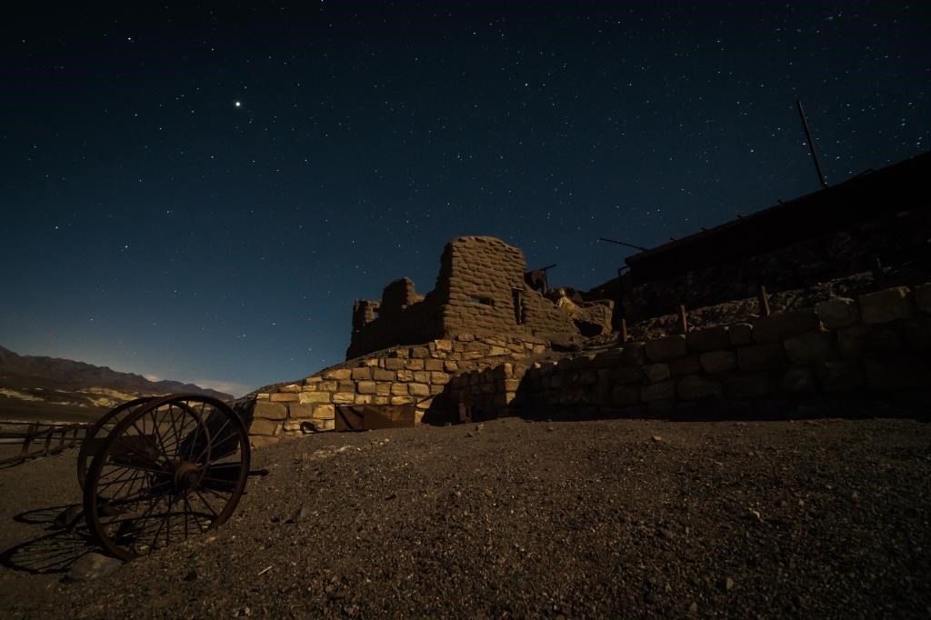 Mining ruins  of an adobe wall and a wagon wheel underneath a starlit sky