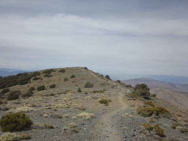 A trail meanders through sparse shrubs and across a rocky ridgeline.