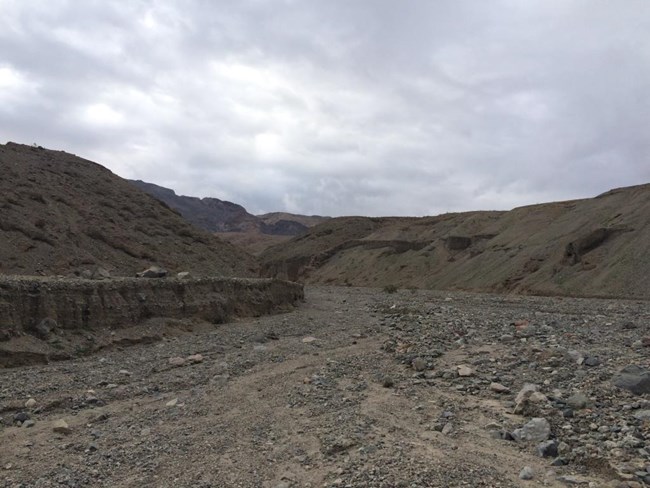 The mouth of a canyon with brown rocky walls and a thick gravel canyon bottom.