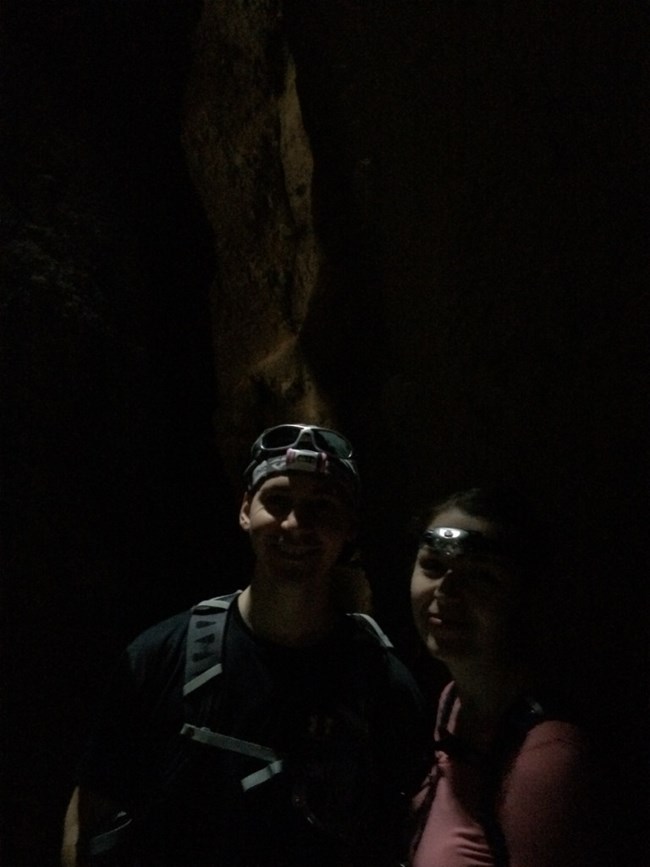 Two hikers with headlamps face camera in dark canyon.