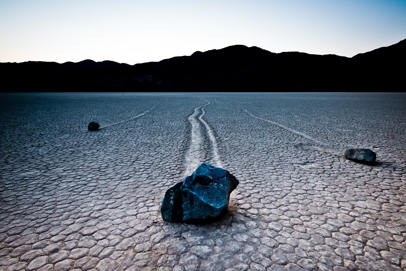 Boulders leave a mysterious trail in the surface of a dry lakebed.