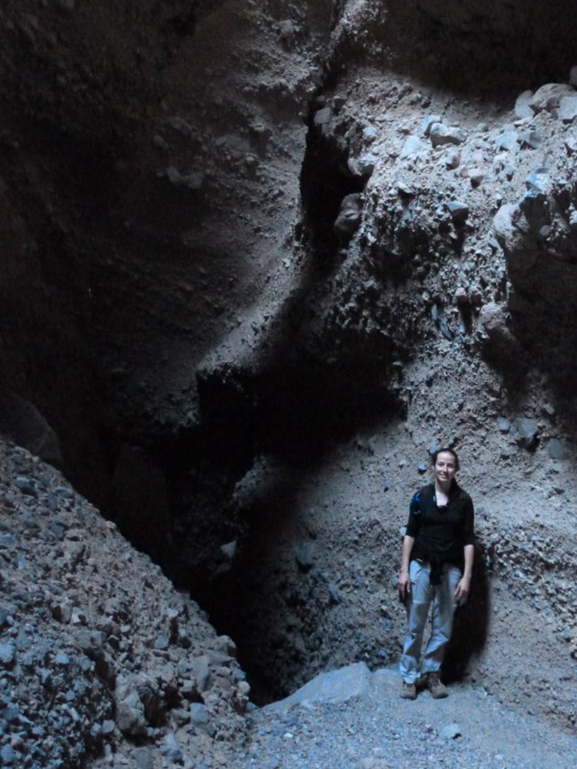 A hiker in a dark slot canyon illuminated by a sliver of light.