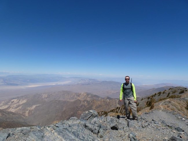 A hiker stands on top of a mountain peak along a narrow ridge.