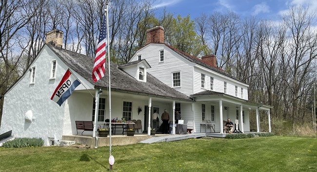 A white house with an open sign and a flag out front. There are people milling around on the front porch.