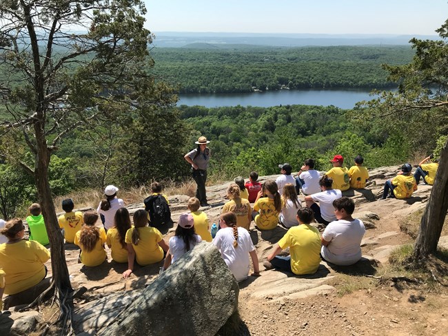 A ranger standing on a rocky outcropping with students during a field trip.