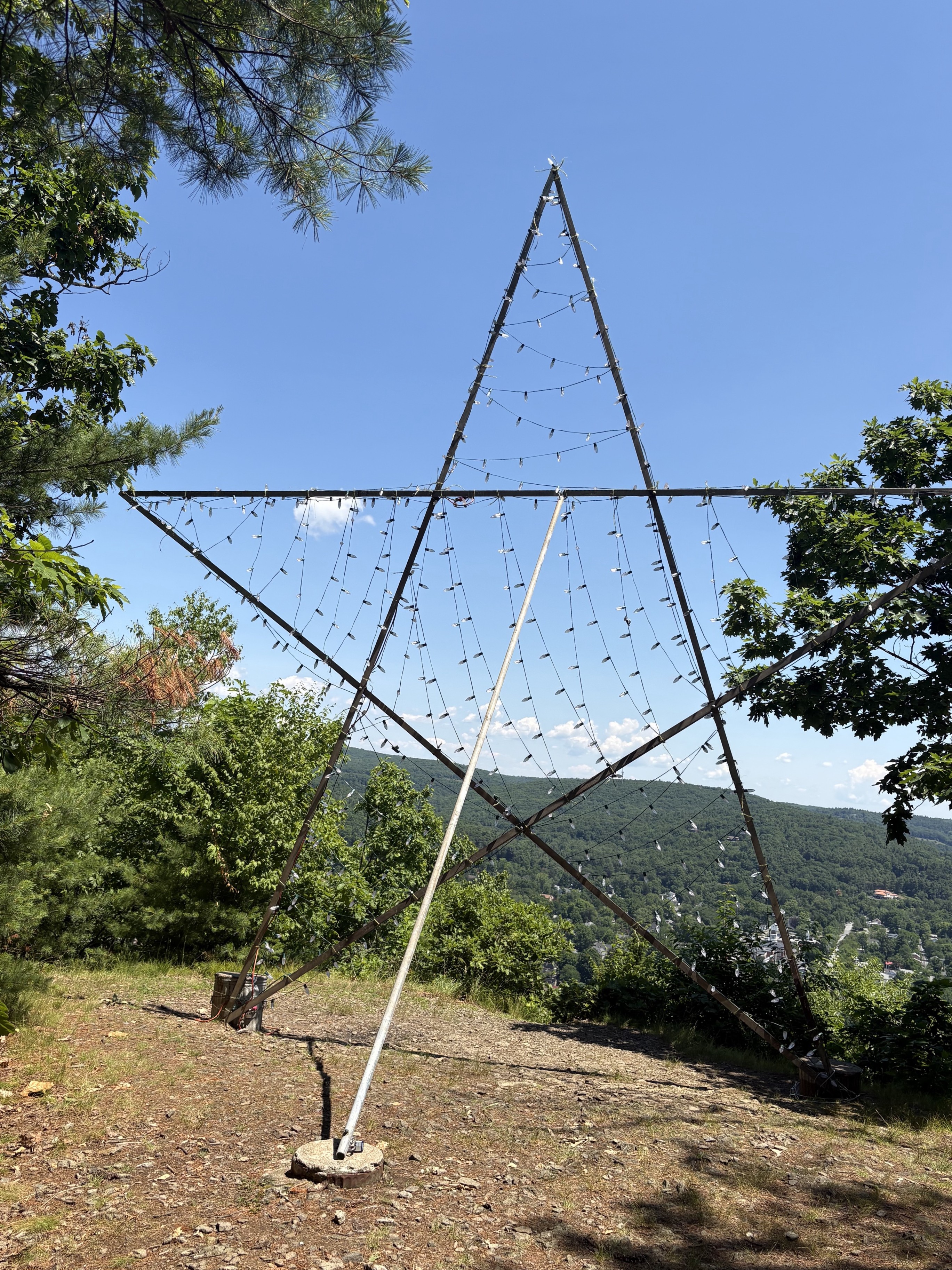 Metal poles in the shape of a star with lights strung between them on a hill overlooking a town.