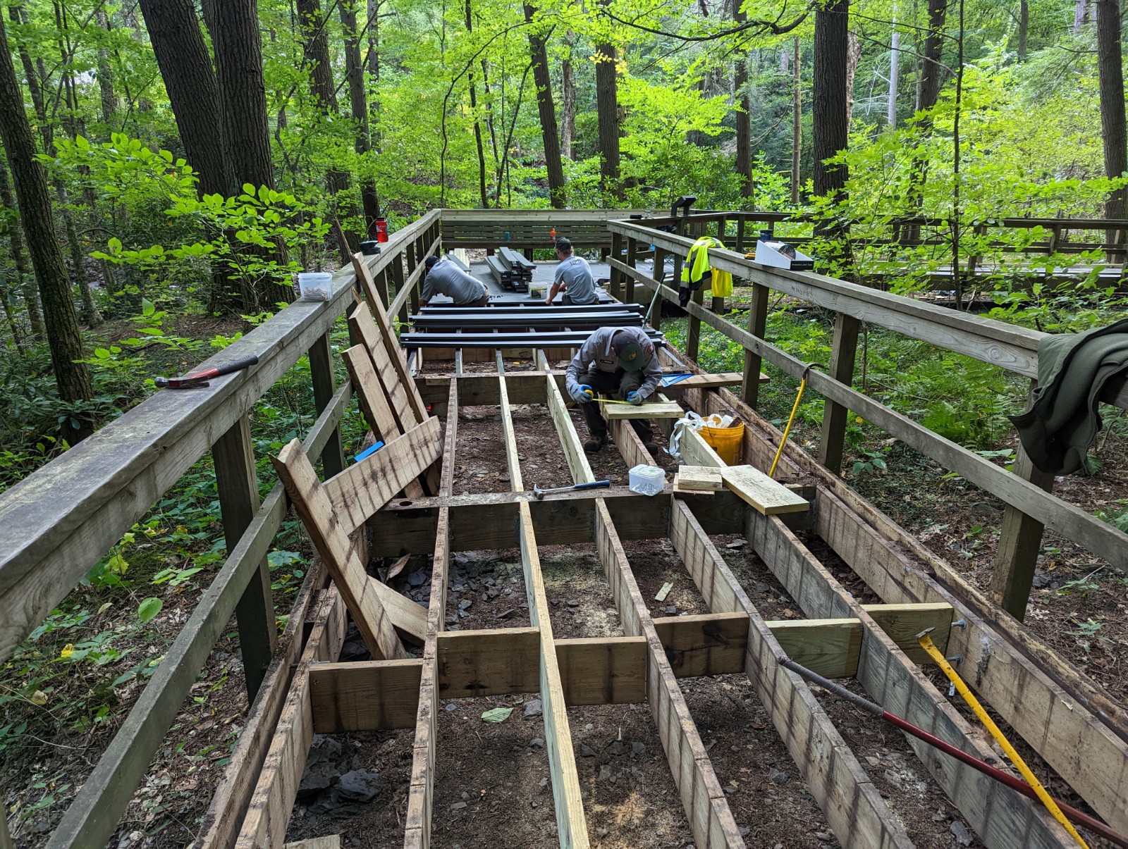 NPS_Trail Crew makes repairs to Dingmans Falls boardwalk_2022 Old boards from the boardwalk trail have been removed while several employees make repairs to the boardwalk's frame and support structures.