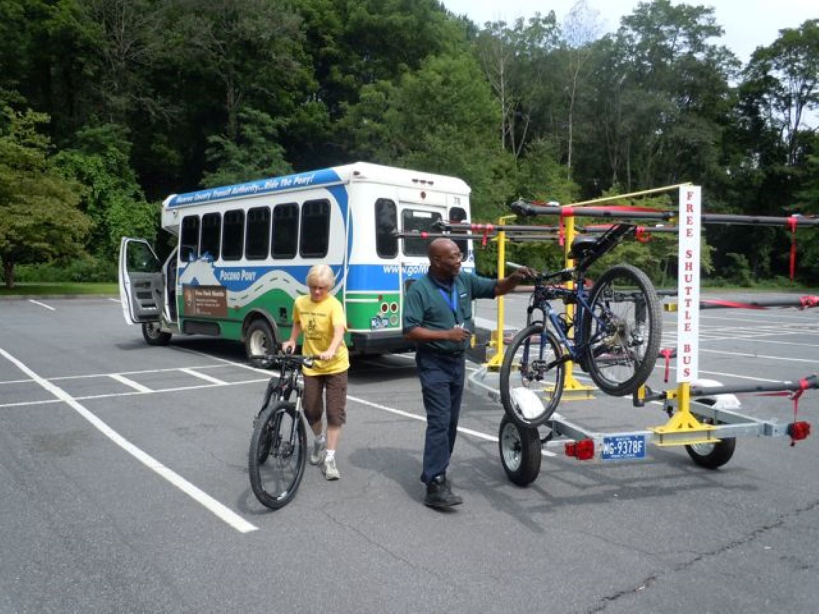 River Runner Shuttle A white, blue, and green shuttle bus towing a trailer with kayaks on it.