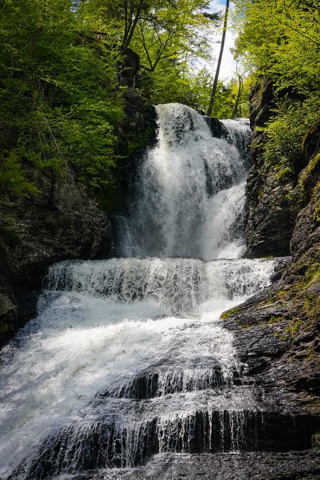 Dingmans Falls flows downward then forward, then downward again, splaying wider as its water hits the creek below