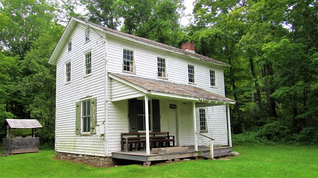 A 19th century house like building with a covered porch and small wooden well house off to the left