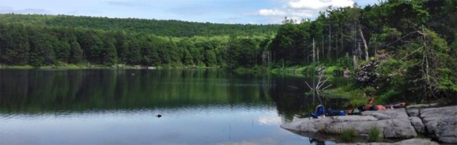 group of people relaxing on a rock that juts out into a lake group of people relaxing on a rock that juts out into a lake