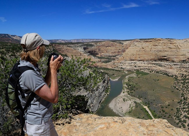 Woman with camera looking into canyon with river below Woman with camera looking into canyon with river below