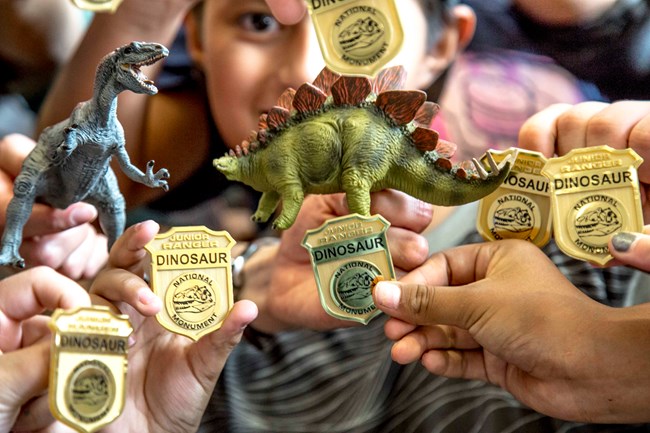Children hold up Dinosaur National Monument Junior Ranger badges and toy dinosaurs.