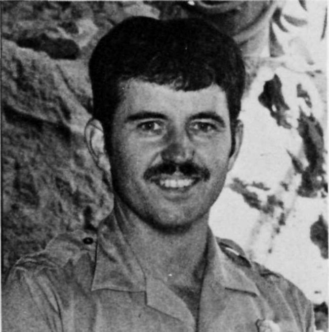 A black-and-white photo of a young man with dark hair smiling at the camera in park service uniform.